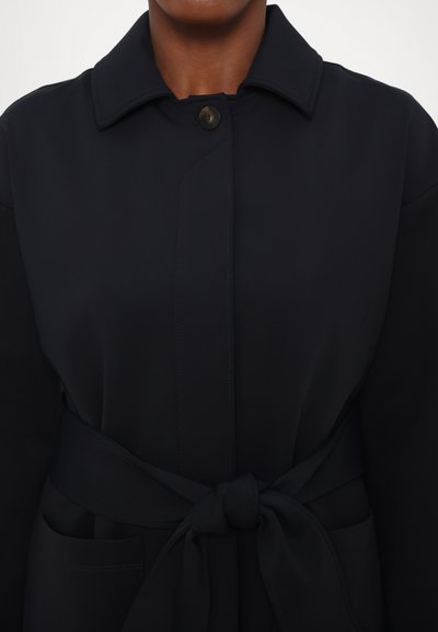 Μπλε ναυτικού παλτό από λεία υφασμά, με κουμπί κλείσιμο, γιακά, ζώνη στη μέση και δύο πλάγιες τσέπες.