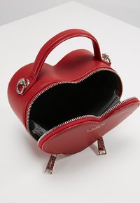 Rode leren handtas in de vorm van een hart, met zilverkleurige hardware, ritssluiting en een interne zwarte voering. Bevat een handvat aan de bovenkant en dubbele accenten aan de onderkant.