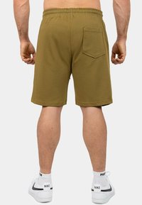 Shorts da allenamento verde oliva con cintura elastica, tasche laterali e una tasca posteriore singola; realizzati in un morbido tessuto testurizzato.