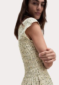 Blumengemustertes Kleid aus weichem, gelbem Stoff. Verfügt über Raffungselemente entlang des Oberteils und kurze, Rüschärmel. Glatte Textur.