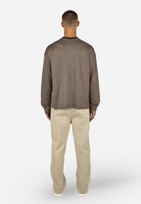 Barna, textúrált, hosszú ujjú ing, laza szabással, hátulról nézve, világos bézs nadrággal és fehér cipővel párosítva.