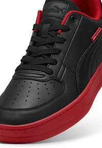 Sorte lædersneakers med rød gummisål, perforeret tåboks og sorte snørebånd. Har Puma-branding og røde detaljer på siden.