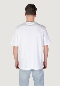 T-shirt bianco in cotone con maniche corte, vestibilità rilassata e colletto rotondo. Tessuto semplice ben visibile; indossata con jeans azzurri chiari.