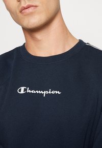 Marineblauwe katoenen sweatshirt met een ronde halslijn, voorzien van het witte 'Champion' logo op de borst en subtiele details op de schouders.