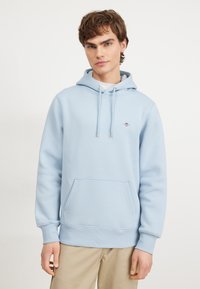 Light blue fleece hoodie with a front pocket, drawstring hood, and ribbed cuffs. Smooth texture with a small embroidered logo on the chest.
