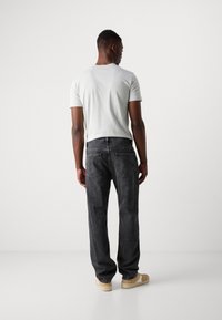 Jeans de mezclilla negra con un corte relajado, un par de zapatos beige y una camiseta de manga corta gris claro, vistos desde la espalda.