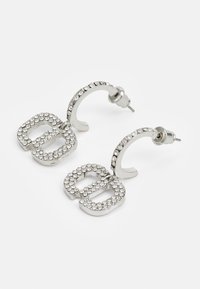 Aretes de aro plateados con un diseño de letras adornado con brillantes strass, que cuentan con un acabado metálico suave y un soporte curvado.