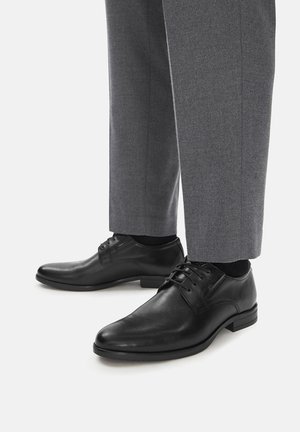 Schwarze Lederschuhe mit elegantem Design, Schnürverschluss und glatter Oberfläche, kombiniert mit maßgeschneiderten grauen Hosen.