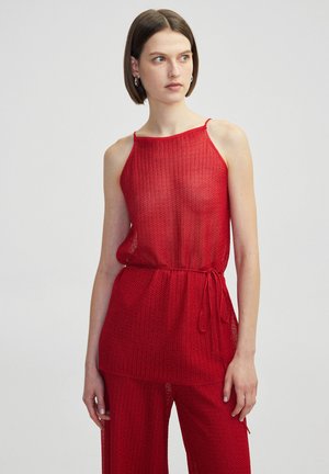 Top sin mangas de punto rojo con un corte holgado, que presenta un patrón texturizado y un detalle de cintura anudada. Fabricado con material ligero y transpirable.