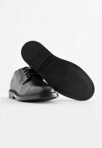 Czarne skórzane buty z okrągłym noskiem, sznurowaniem oraz teksturowaną gumową podeszwą dla lepszej przyczepności, o gładkich powierzchniach i minimalnych detalach szwów.