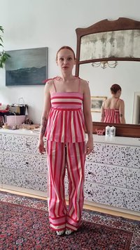 Top senza maniche a righe rosa e bianche con spalline a fiocco abbinato a pantaloni larghi a righe; entrambi hanno una vestibilità rilassata e una trama fresca.