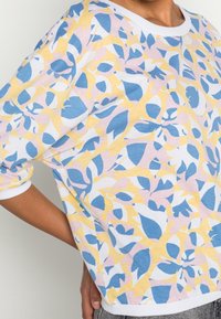 Felpa a maniche corte in morbido cotone, caratterizzata da un motivo floreale colorato nei toni del blu, rosa e giallo, con colletto e polsini a costine bianchi.