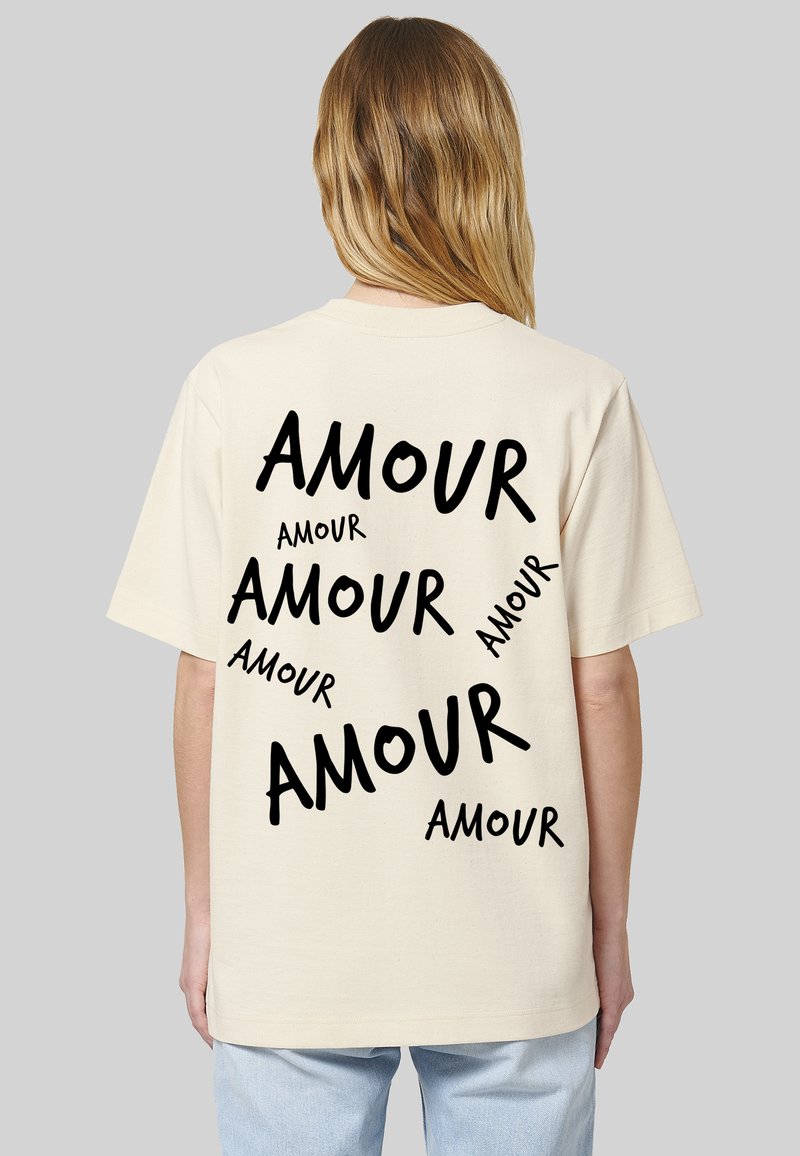 T-shirt en coton beige avec une coupe décontractée, présentant plusieurs textes stylisés en noir "AMOUR" de tailles variées au dos.