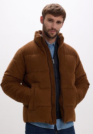 Giacca puffer in corduroy marrone con colletto alto, chiusura a zip e tasche laterali, indossata sopra una camicia di jeans azzurro chiaro.