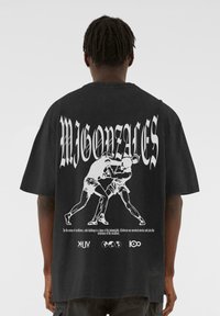 Sort oversized t-shirt med et hvidt grafisk tryk af to boksere og tekst. Korte ærmer og rund halsudskæring.