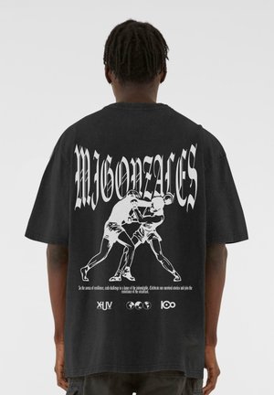 Black oversized t-shirt featuring a white graphic of two boxers and text. Short sleeves and a round neck design.