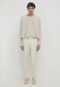 Maglione a maglia crema con texture a coste, abbinato a pantaloni bianchi su misura. Scarpe slip-on color cammello completano l'outfit. Design semplice e coerente.