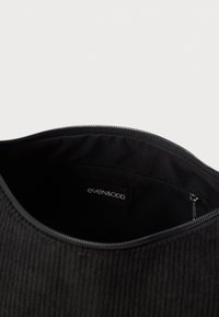 Borsa in corduroy nera con chiusura a zip, caratterizzata da una superficie texturizzata e un'etichetta interna che recita "even&odd."