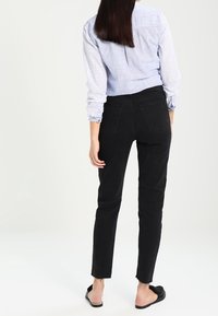 Svarta denim skinny jeans med hög midja, bakfickor och rå kant. Matchas med en ljusblå randig skjorta med knappar.