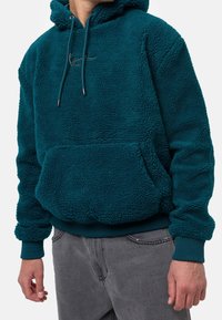 Sudadera de forro polar en color azul verdoso con un bolsillo tipo canguro, puños y dobladillo acanalados; cuenta con un cordón ajustable y un logo sutil en la parte delantera.