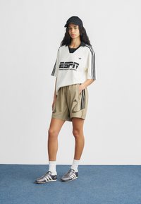 Fehér, túlméretezett ing fekete ESPN logóval, fekete gallérral és három fekete csíkkal. Khaki rövidnadrág oldalzsebekkel. Szürke sportcipő fehér díszítéssel.