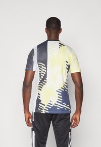 T-shirt de sport à manches courtes présentant un motif abstrait audacieux en noir, blanc et jaune avec une finition texturée. La vue arrière montre un dégradé de couleurs.