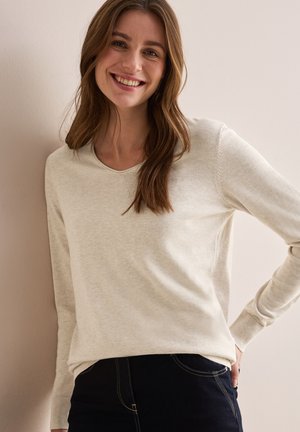 Helles beiges Sweatshirt mit Rundhalsausschnitt und langen Ärmeln. Weicher Stoff mit gerippten Bündchen, kombiniert mit dunklen Jeans. Schlichtes, lässiges Design.