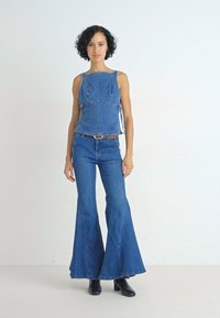 Denimoutfit met een fitted, mouwloos topje en uitlopende broek in middelblauw. De stof heeft een klassieke textuur met zichtbare stikseldetails.