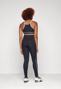 Black sports bra with white trim, paired with high-waisted black leggings featuring a white side stripe. Model wears white athletic shoes.