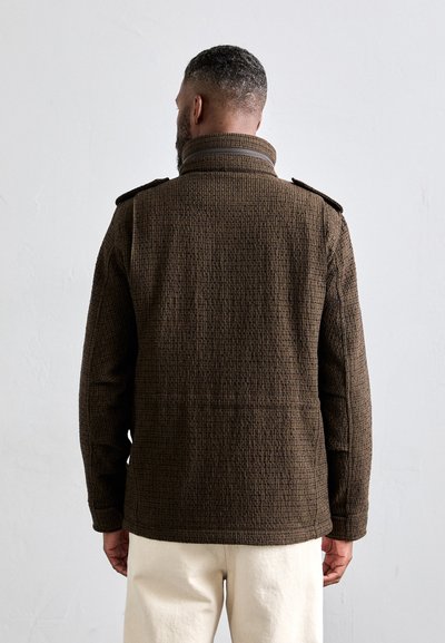 Veste marron texturée avec un col haut et des épaulettes aux épaules, conçue avec un motif tissé et une coupe décontractée.