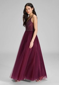 Burgundowa sukienka wieczorowa z beaded bodice, cienkimi ramiączkami i zwiewną tiulową spódnicą. Charakteryzuje się dopasowaną talią prowadzącą do długości pełnej.