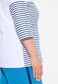 Gestreiftes Oberteil mit Dreiviertelärmeln, mit weißen und dunkelblauen horizontalen Streifen, kombiniert mit blauen Hosen. Weicher Baumwollstoff.