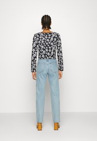 Top preto de mangas compridas com padrão floral branco, combinado com jeans de cintura alta de cor azul clara e sapatos de salto bloco castanhos.
