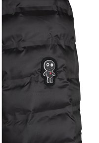 Schwarze Puffy-Jacken-Sektion mit einer gestickten schwarz-grauen Cartoonfigur mit einem Auge und einem roten Herzen auf der Brust, vor glattem Stoff.