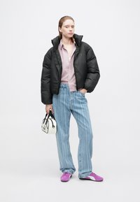 Čierna páperová bunda, svetloružová košeľa s gombíkmi, svetlomodré pásikavé džínsy, fialové a biele topánky a malá biela kabelka s čiernymi akcentmi.