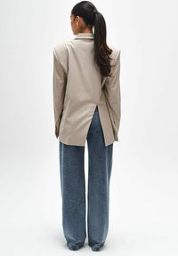 Beige oversized blazer met schoudervullingen en een rugsplit, gecombineerd met losse blauwe spijkerbroeken. Gladde textuur, minimale details.
