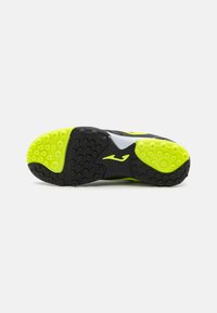 Suela de zapatilla deportiva en negro y verde neón con un patrón texturizado de agarre, que presenta un logo blanco y un dibujo en forma de hexágono para tracción.