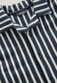 Navy och krämrandig stickad skorta med krage, knappslå, texturerat tyg och kontrasterande knappar.