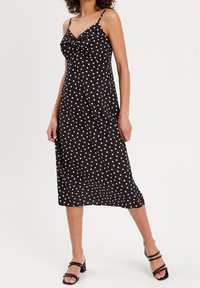 Sort midi-kjole med hvide polkaprikker, med justerbare tynde stropper og en samlet frontdetalje. Glat stof med en flydende silhuet.