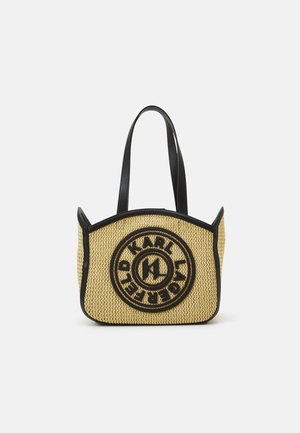 Beigenvärinen punottu käsilaukku mustilla reunoilla, pitkät mustat kahvat ja pyöreä "Karl Lagerfeld" -logo edessä.