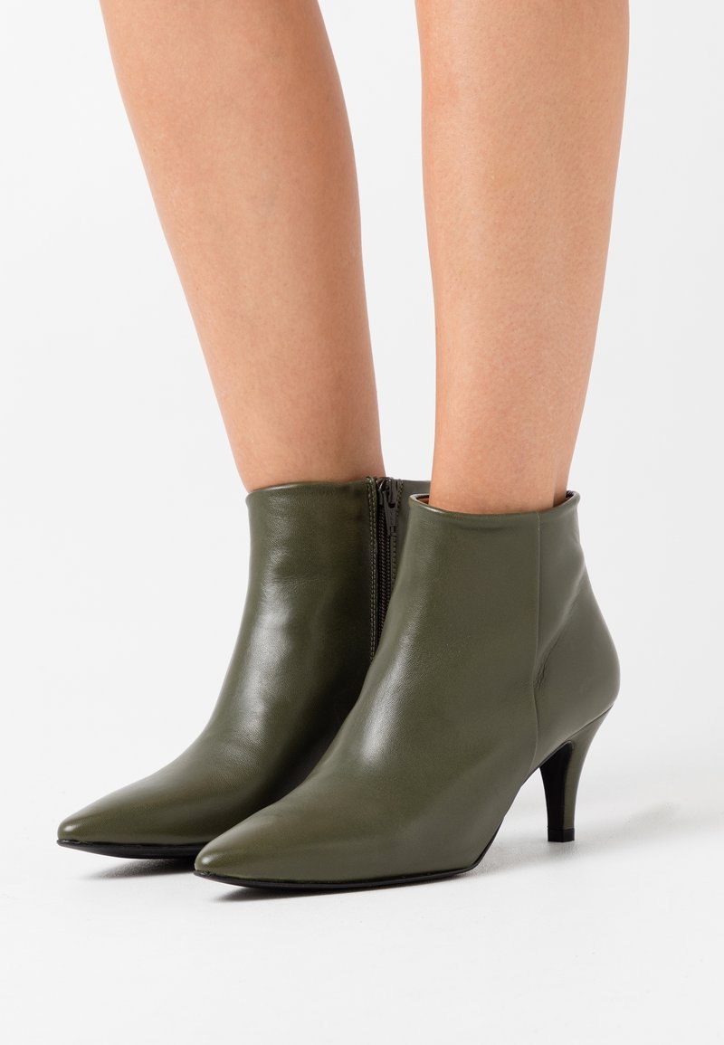 Olivgrüne Leder-Stiefeletten mit spitzer Zehenpartie, seitlichem Reißverschluss und schlankem, niedrigem Absatz, mit glatter Textur und minimalen Details.