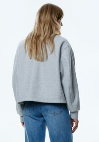 Geknipte grijze sweatshirt met een zachte textuur, brede mouwen en geribde boorden, gecombineerd met hoge taille blauwe denim jeans.
