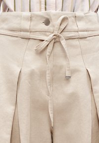 Μπεζ παντελόνι με ψηλή μέση και υφή, διαθέτει ζώνη από ύφασμα για δέσιμο και μεταλλικό κουμπί κλεισίματος στη μέση. Πτυχώσεις για στυλ.