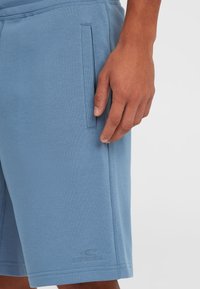 Shorts bleu clair fabriqués en tissu doux, avec une poche latérale et des coutures visibles. Un logo "O'Neill" est subtilement embossé près de l'ourlet.