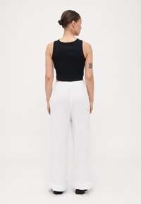 Black cropped tank top paired with loose white wide-leg pants. The pants have a textured fabric and contrasting cuffs at the hem.
