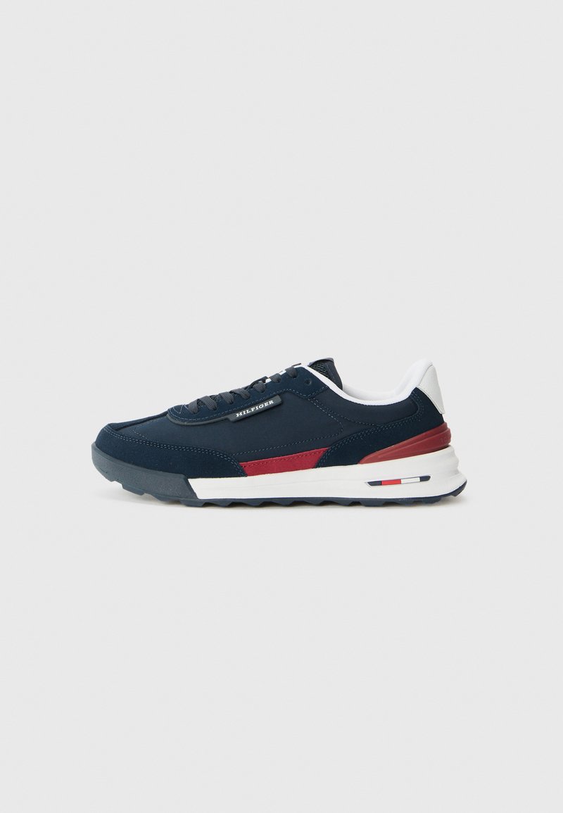 Sneaker blu navy con materiali in camoscio e rete, accenti rossi, tallone bianco e suola in gomma bianca. Presenta lacci piatti e dettagli cuciti.