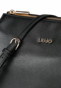 Zwarte leren handtas met een gestructureerde afwerking, gouden rits en LIU JO-logo in gouden accenten. Voorzien van een smalle verstelbare band.