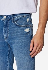 Blekta blå denimjeans med synliga revor på framsidan, femficksdesign och standard midja. Silverdetaljer vid midjan.