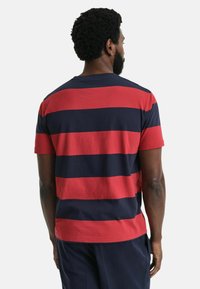 Gestreiftes Baumwoll-T-Shirt mit abwechselnden roten und marineblauen horizontalen Streifen, kurzen Ärmeln und Rundhalsausschnitt.