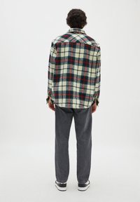 Flanelová košile s kostkovaným vzorem v zelené, červené a krémové barvě. Košile má límec, manžety na knoflíky a uvolněný střih. Kombinováno se šedými kalhotami.